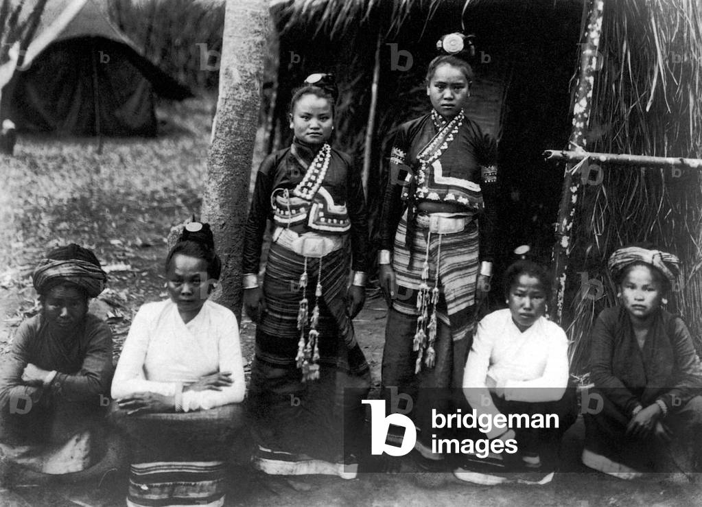 Burma / Myanmar: Six Tai Lu women from Mong Lay in Shan state pose for a photograph in 1909. The two in the middle are in festive costume; the two in white pinafores wear city attire; and the two squatting on the outside are in peasant dress
