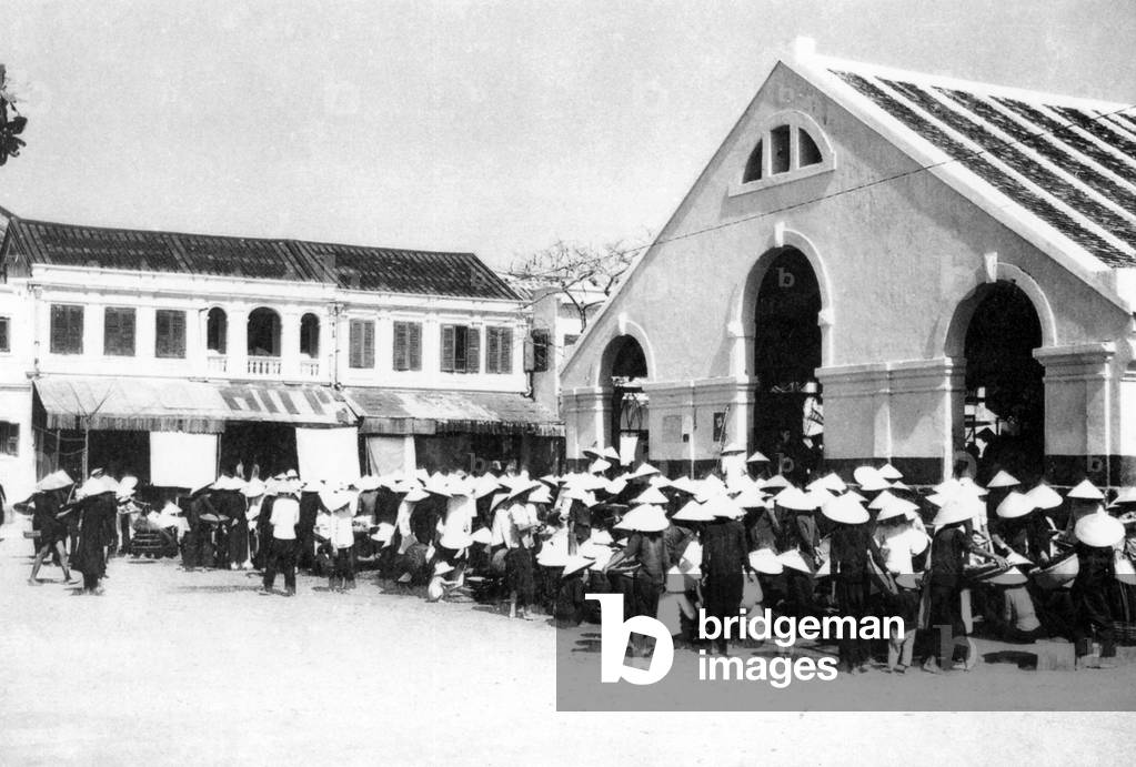 Vietnam: Vendors in their non la (Vietnamese conical hats) cluster in front of the Hoi An main fresh market, Hoi An (c. 1950)