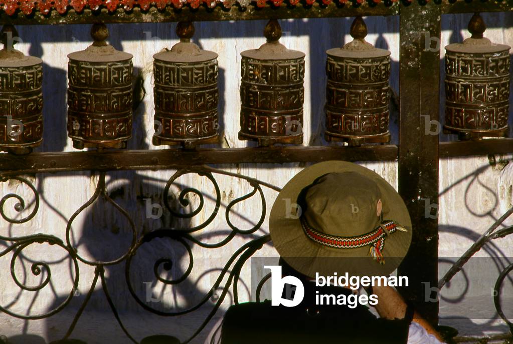 Nepal: Tibetan pilgrim in front of prayer wheels at Bodhnath (Boudhanath), Kathmandu