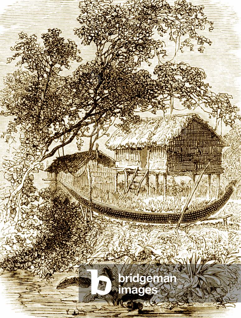 Laos/ Cambodia: A long pirogue stands in front of a traditional house on stilts by the banks of the Mekong River.