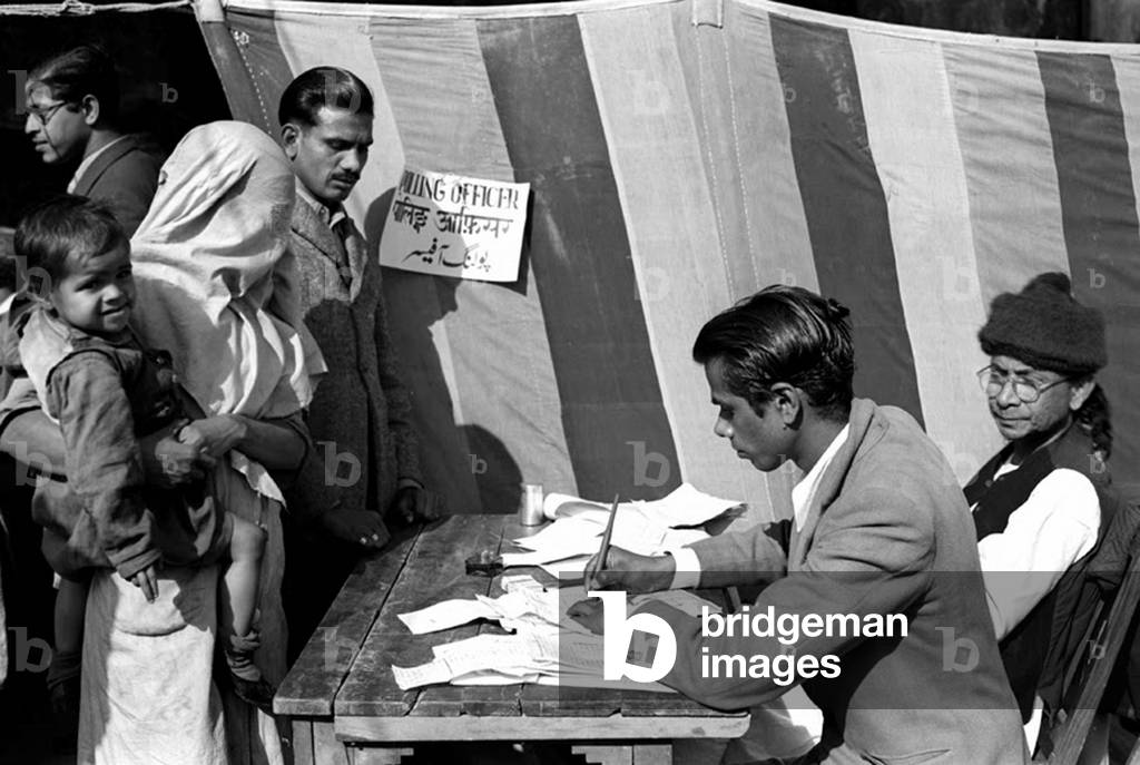 India: First Lok Sabha general election, Delhi, January 1952. A veiled Muslim woman carrying her child casts her vote at a polling station near the Jama Masjid (Friday Mosque) in Old Delhi