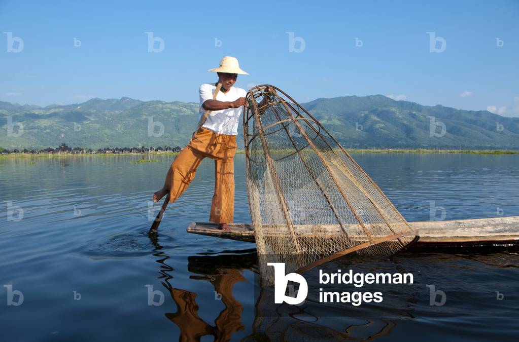 Burma / Myanmar: A leg rowing Intha fisherman shows off his skills with a large conical fish trap at Inle Lake, Shan State