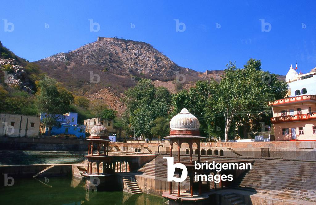 India: The walled fortifications of the Bala Qila (Alwar Fort) loom above the huge kund (tank) next to the Vinay Vilas (City Palace), Alwar, Rajasthan