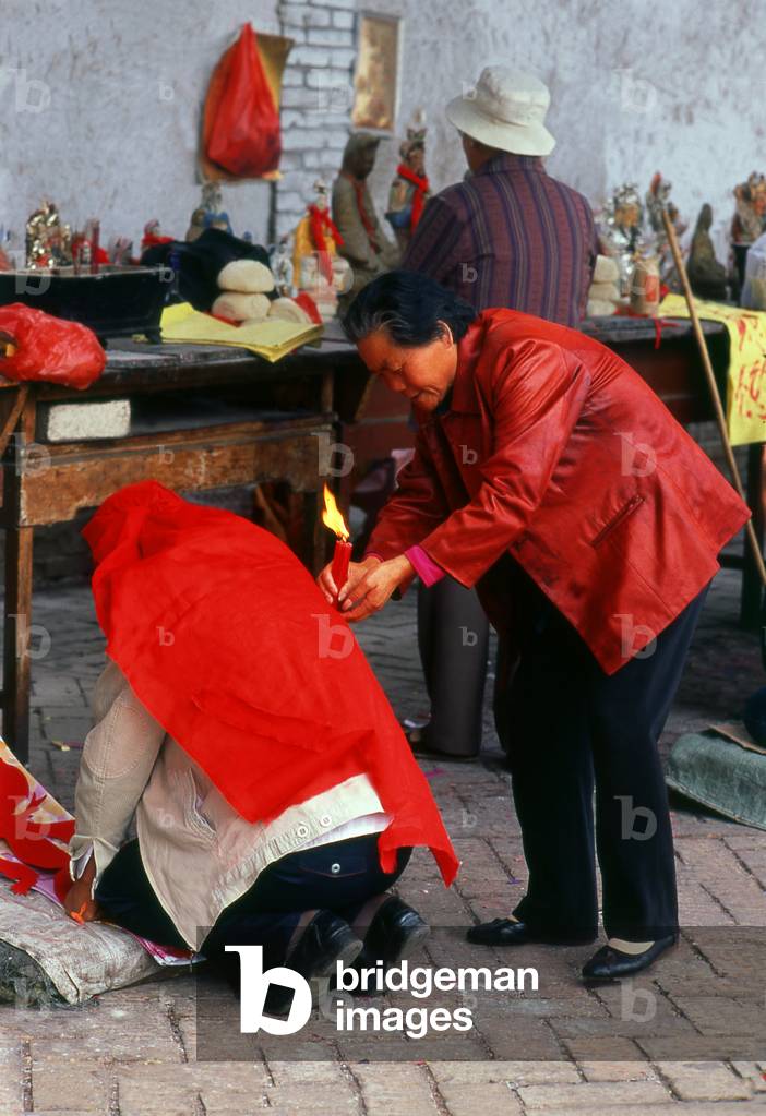 China: Taoist medium dousing with ceremonial flame, Dayun Si (Dayun Temple), a Tang Dynasty (618 - 907 CE) temple, Wuwei, Gansu Province. Taoist rites are performed, with mediums covering supplicants with red cloths, ringing bells and shaking censers