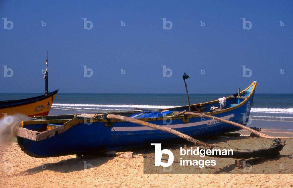 India: A traditional Goan outrigger fishing boat sits on the beach at Benaulim Beach, South Goa