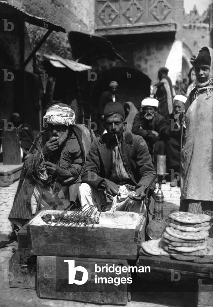 Palestine: Palestinian kebab and flatbread seller with customers in a Jerusalem market, c. 1910