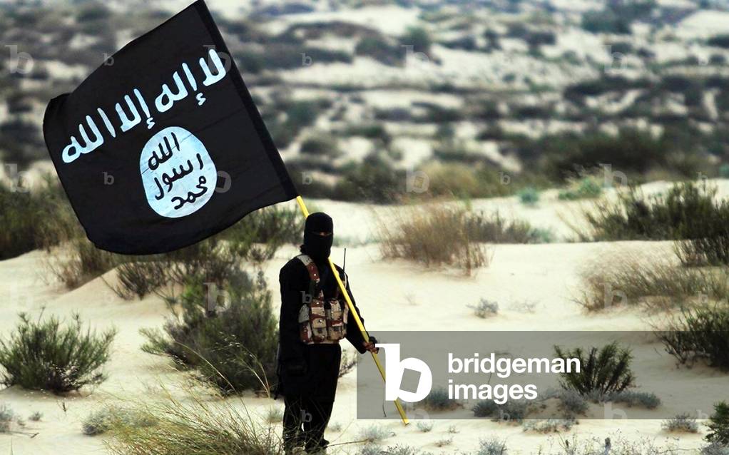 Islamic State / Iraq / Syria: A masked Islamic State soldier poses holding the ISIL banner somewhere in the deserts of Iraq or Syria. ISIL publicity image, 2015