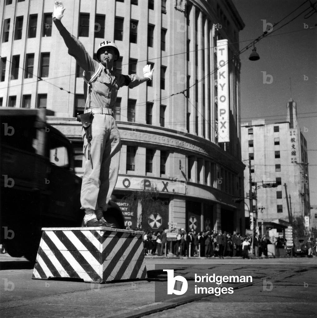 Japan: US Military Policeman on traffic duty in Ginza, Tokyo, Tokyo Post Exchange in the background. Ken Domon (1909 - 1990), 1946