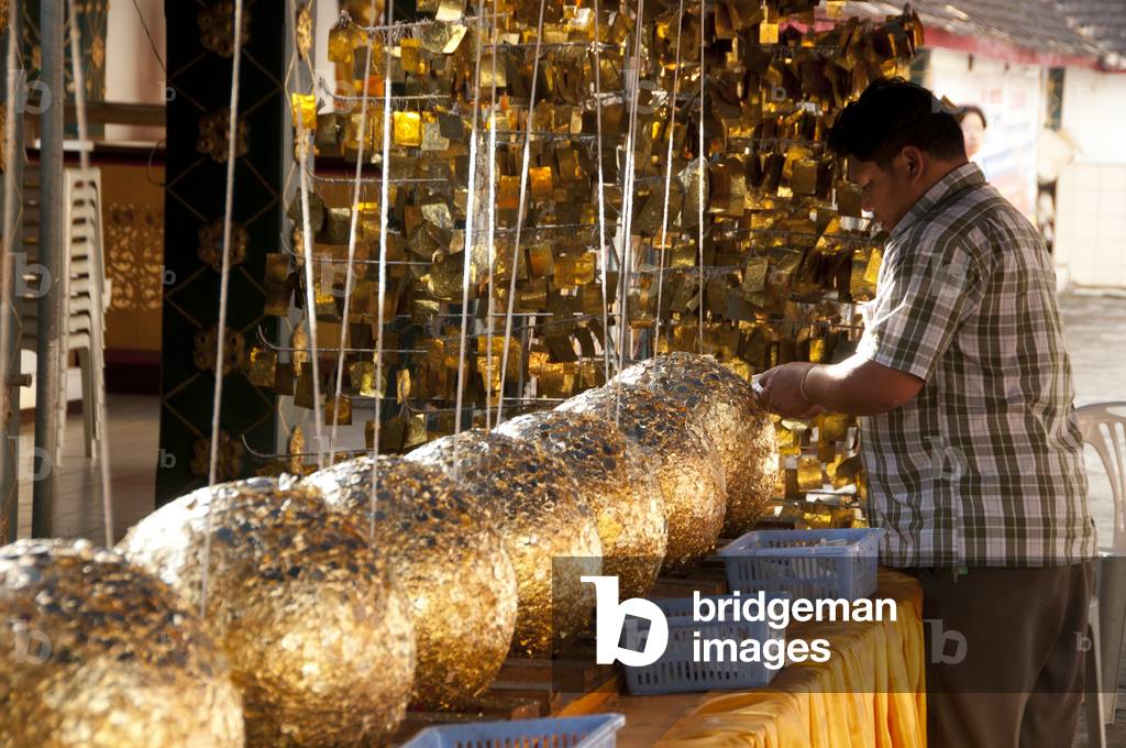 Thailand: A man plasters gold leaf on luk nimit (holy stone spheres), Wat Phrathat Doi Kham, Chiang Mai