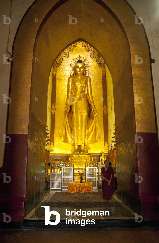 Burma / Myanmar: A Buddhist monk in front of the standing Buddha Konagamana in the central niche facing east, Ananda Temple, Bagan (Pagan) Ancient City