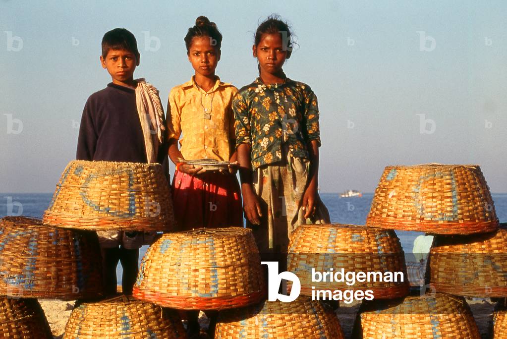 India: Children from the local fishing community stand behind fish baskets at Colva Beach, Salcete, south Goa