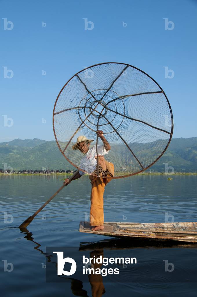 Burma / Myanmar: A leg rowing Intha fisherman shows off his skills with a large conical fish trap at Inle Lake, Shan State