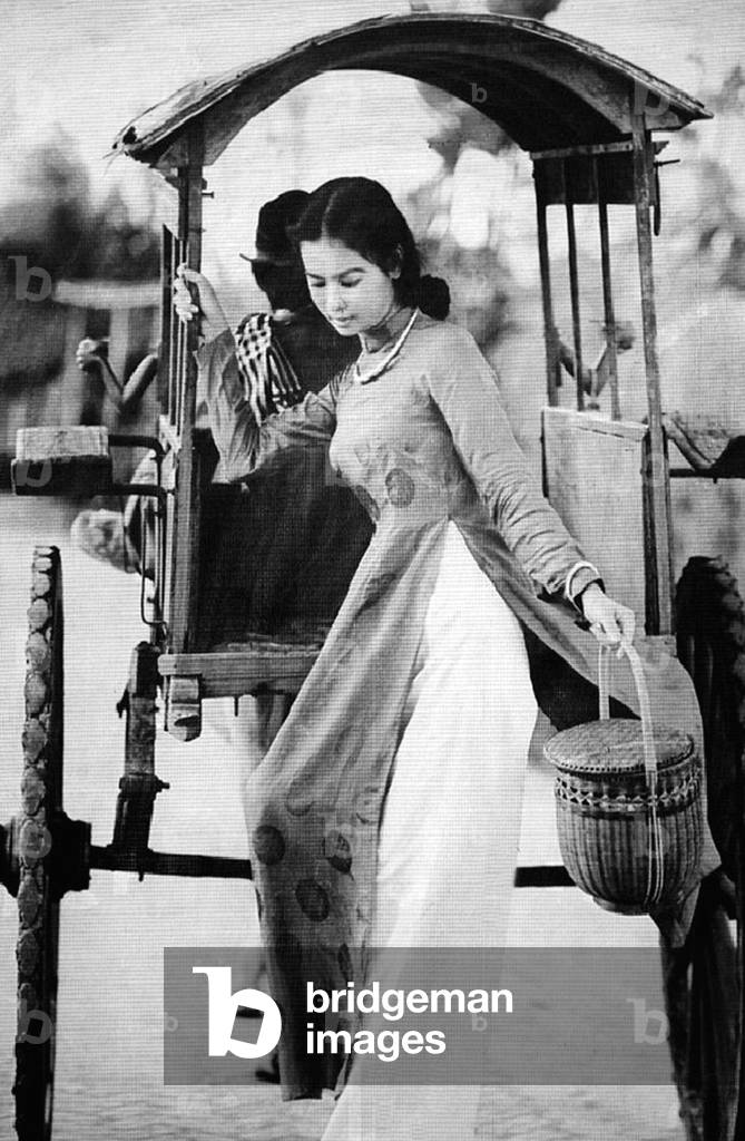 Vietnam: Young woman in an ao dai dress descending from a covered pony cart, Saigon, 1950s