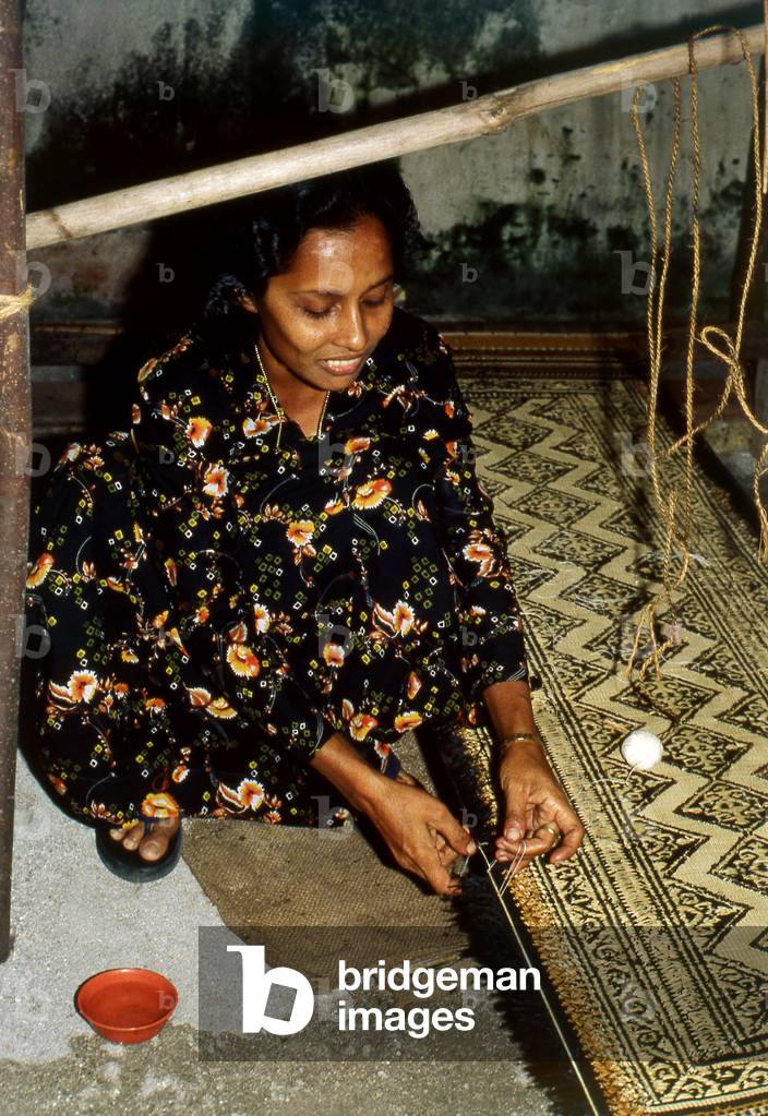Maldives: A weaver stitching a fringe to a grass 