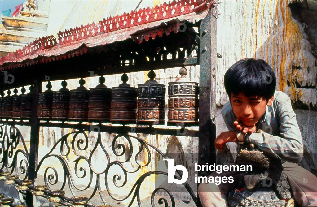 Nepal: A boy poses next to prayer wheels at Swayambhunath (Monkey Temple), Kathmandu Valley