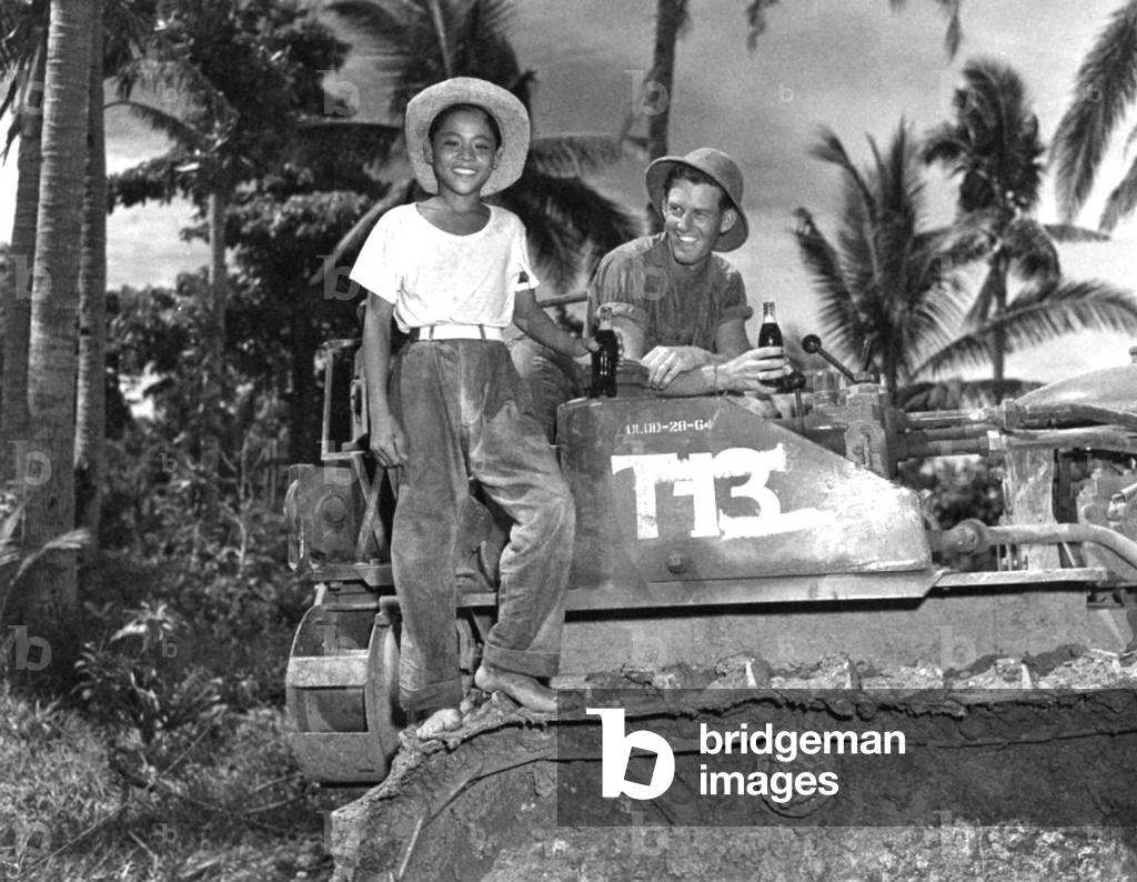 Philippines / USA: A young Filipino boy and an American bulldozer operator of the 64th Seabees (United States Naval Construction Forces, or NCF) enjoy a cold drink following the Battle off Samar, Leyte Gulf Campaign, October 1944 (photo)