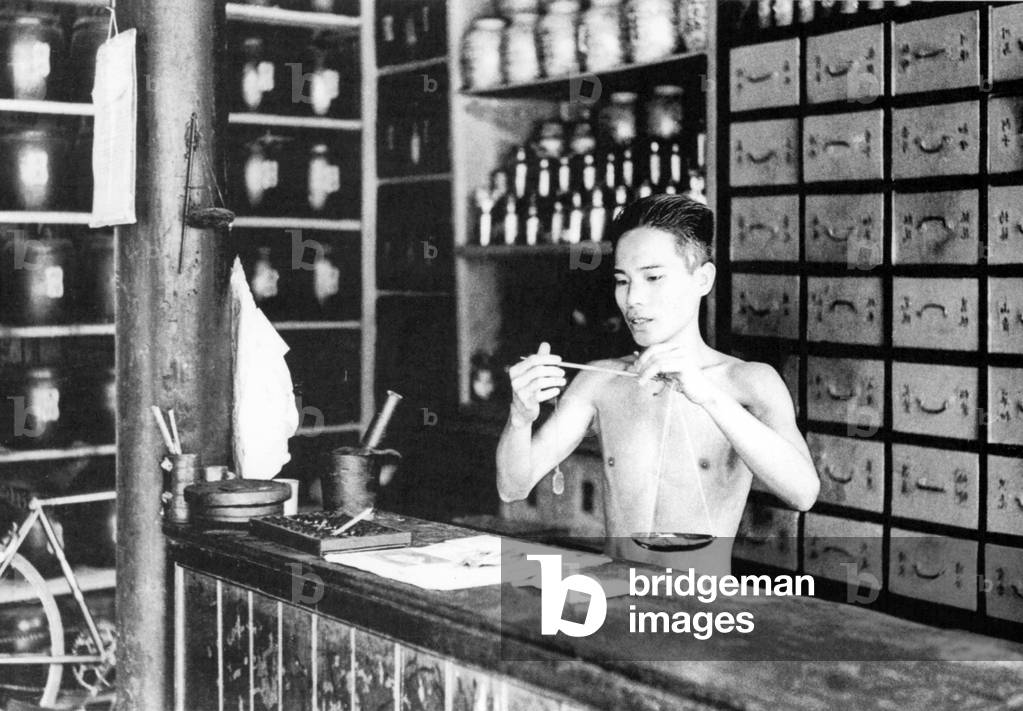 Vietnam: Weighing out medicinal products in a Chinese medicine shop, Hoi An (1950)
