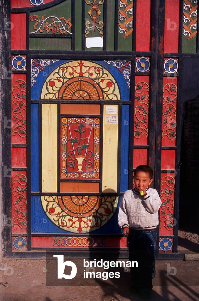 China: Young boy in front of his home's brightly decorated doors in Old Kuqa, Xinjiang Province