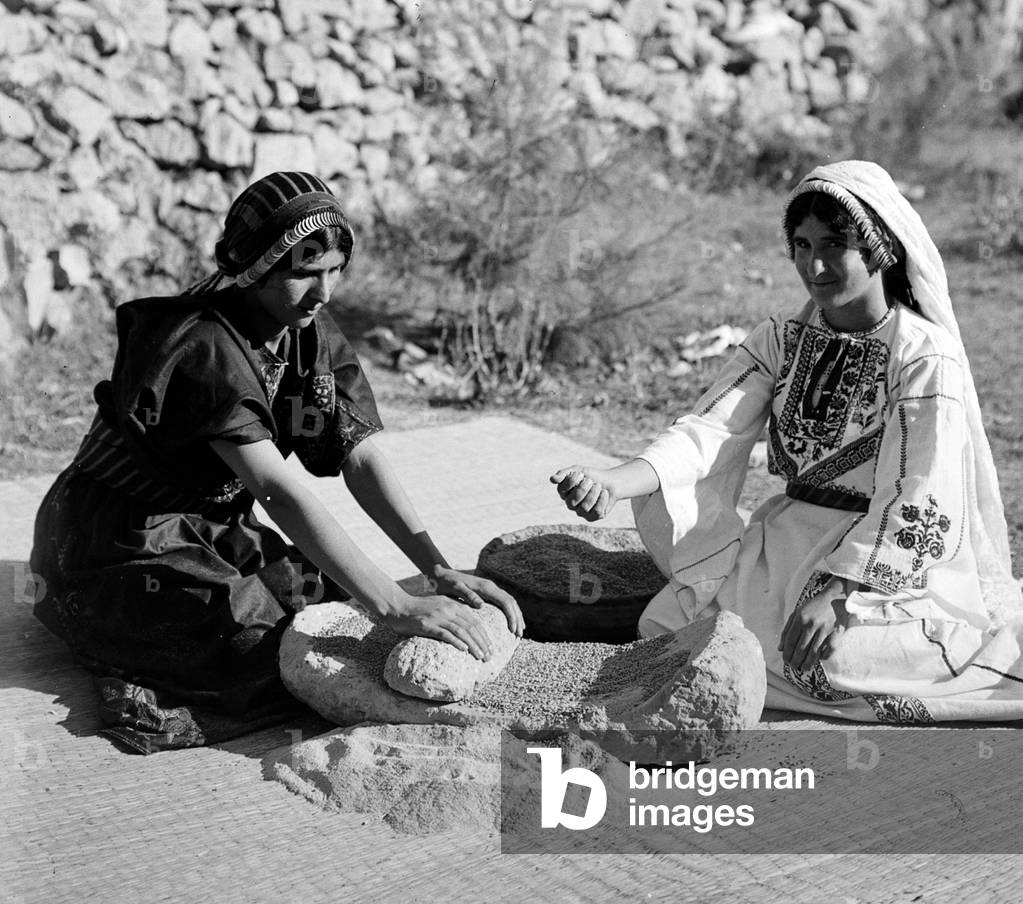 Palestine: Two Palestinian women grinding wheat, c. 1920