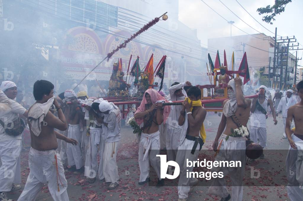 Thailand: Shop owners wave bamboo poles with strings of exploding firecrackers over the heads of shrine bearers, Phuket Vegetarian Festival