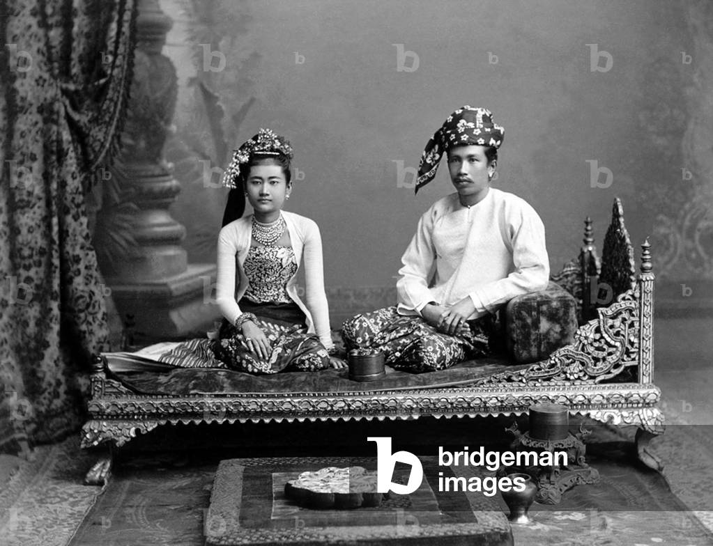 Burma / Myanmar: Studio portrait of a well-to-do Burman couple on a Burmese bed, probably Rangoon / Yangon, c. 1890s. Philip Adolphe Klier (c.1845-1911)