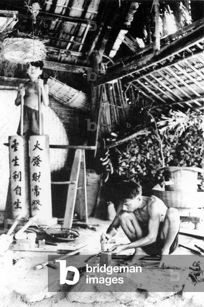 Vietnam: A blacksmith with his assistant using Chinese-style bellows in Hoi An (1950)