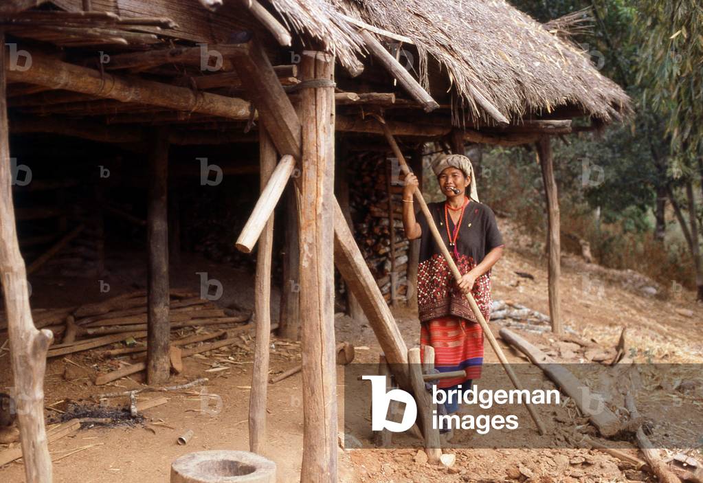Thailand: A Karen woman stands, pipe in mouth, outside her house, near Mae Sariang, Mae Hong Son Province, northern Thailand