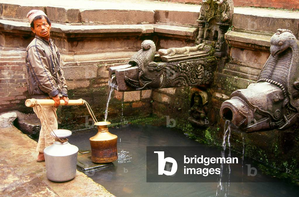 Nepal: A man fills his water pots at the Tusha Hiti, a well lined with a profusion of stone carvings in the Sundari Chowk or 'Courtyard of Beauty' within the Royal Palace, Patan, Kathmandu