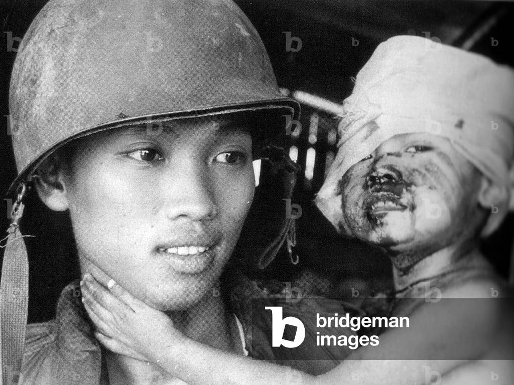 Vietnam: Army of the Republic of Vietnam (ARVN) soldier holding a wounded baby boy, Saigon, 1975 (b/w photo)