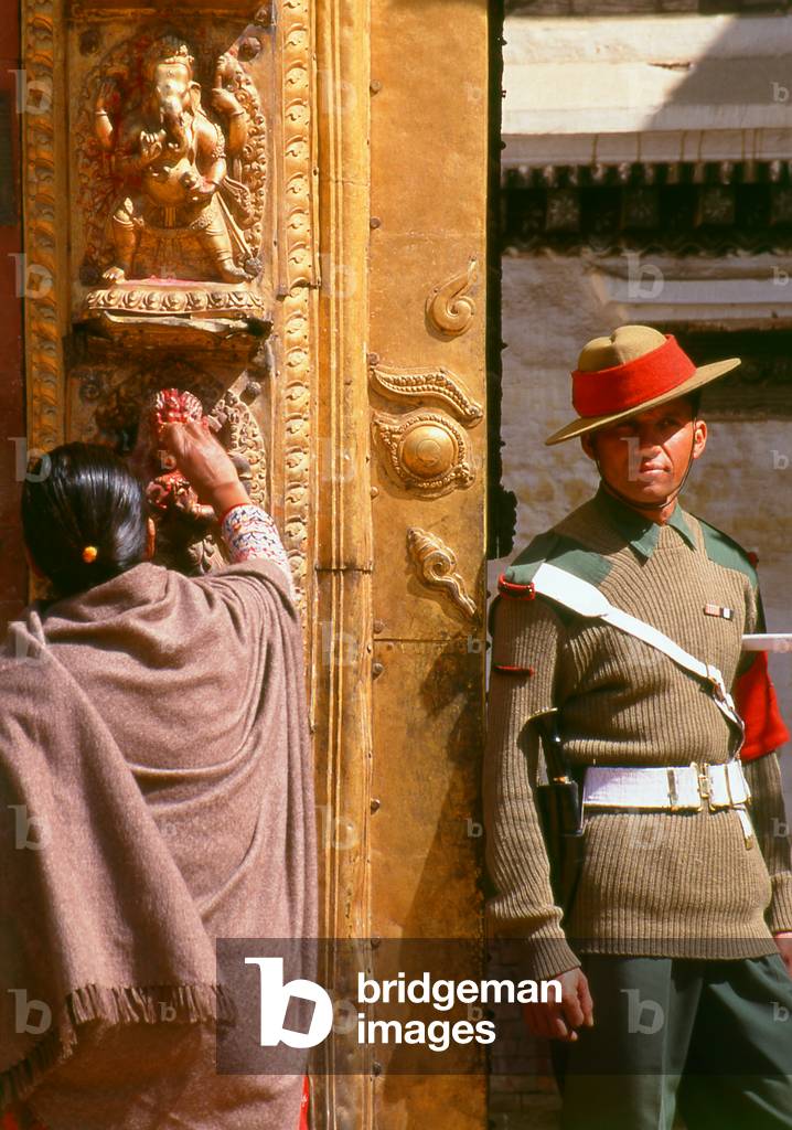 Nepal: A soldier guards the Golden Gate (Sun Dhoka) leading to the Taleju Temple within the Royal Palace complex while a woman pays homage to a deity, Bhaktapur, Kathmandu Valley (1997)