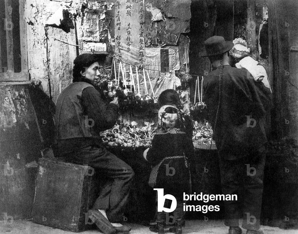 USA: Chinese man with queue and three children at a roadside toy stall, San Francisco Chinatown, c. 1900