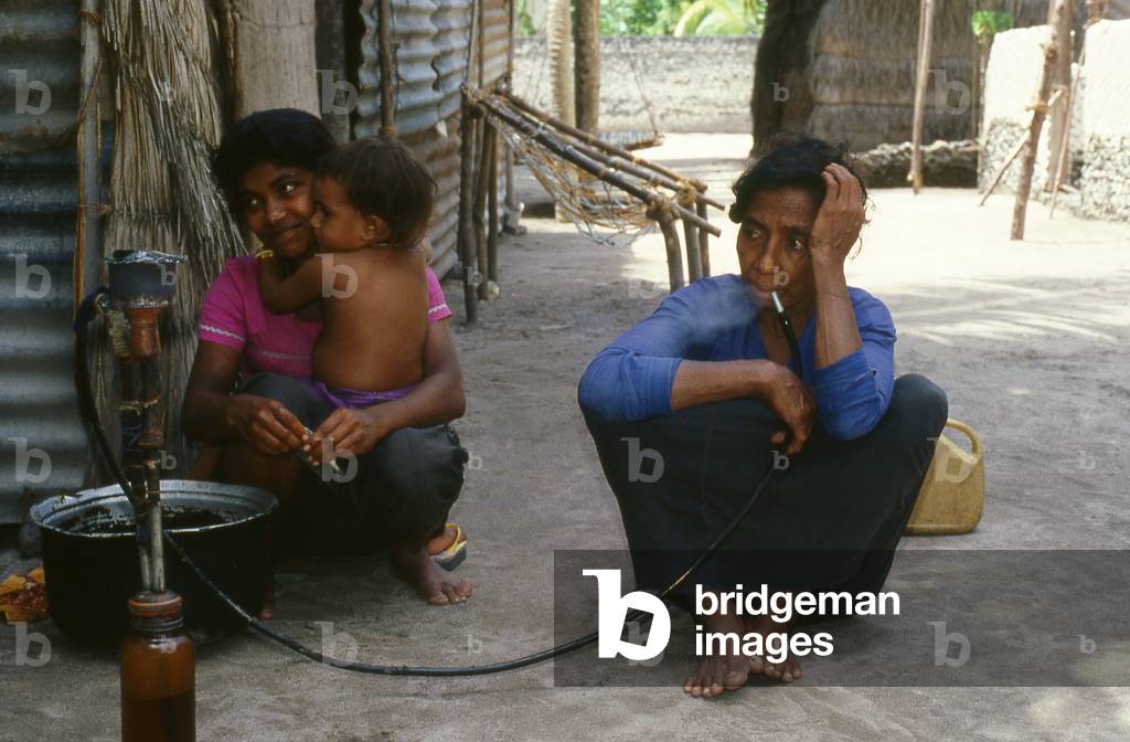 Maldives: A woman smoking a traditional hookah (shisha) pipe, Addu Atoll (Seenu Atoll) 1980