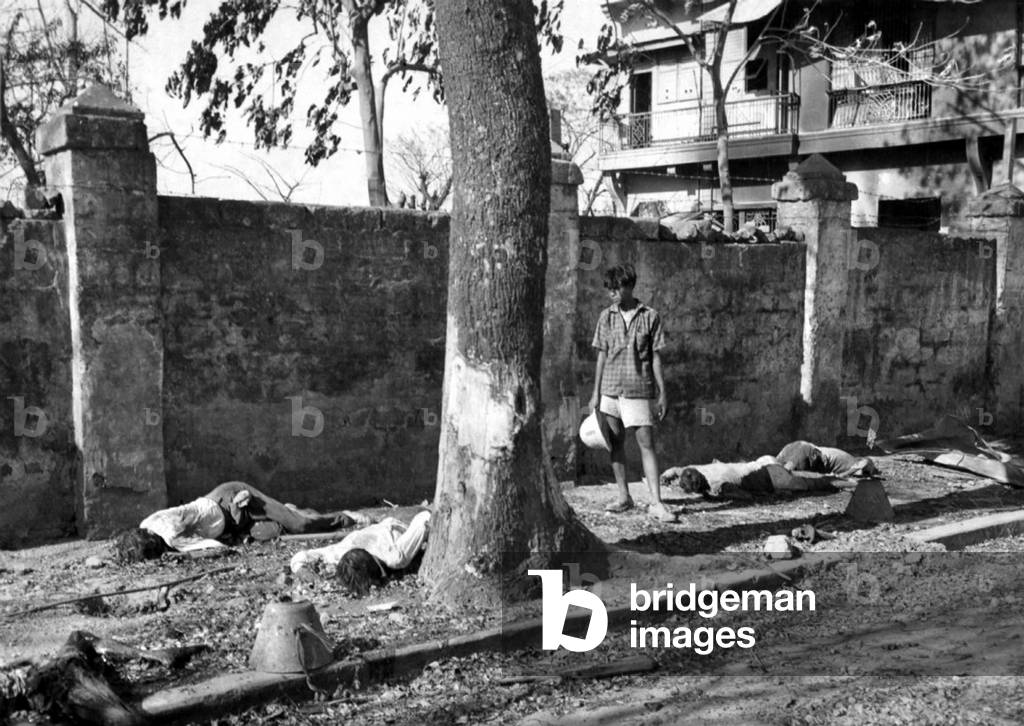 Philippines: A Filipino civilian looks at the bodies of people killed in the Ermita district during the Battle of Manila, March 1945 (photo)