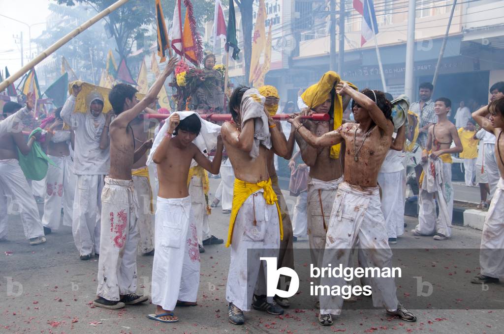 Thailand: Shop owners wave bamboo poles with strings of exploding firecrackers over the heads of shrine bearers, Phuket Vegetarian Festival