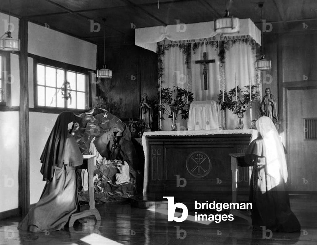 Korea: Convent altar, Heijo (Pyongyang) ca. 1939. Two Sisters kneel in front of the convent altar decorated for Christmas. To the left of the altar is a nativity scene behind which stands an evergreen tree. A Chi-Rho adorns the altar
