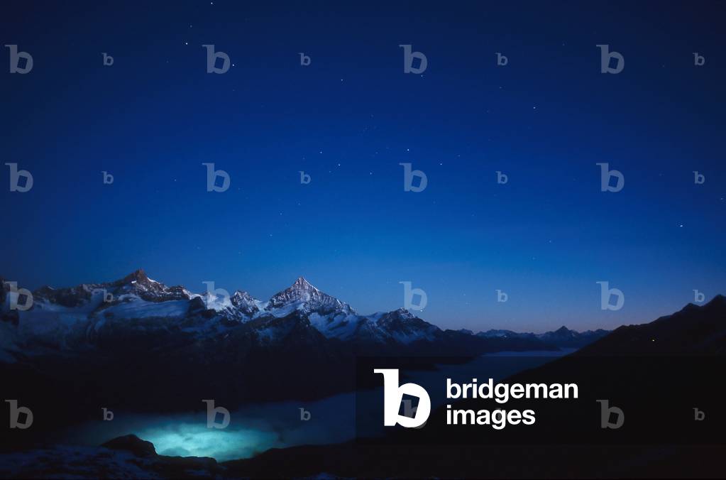 Star sky above Weisshorn - Starry sky above Weisshorn - Star sky above Weisshorn in the Swiss Alps seen from Gornergrat. Moonlight illuminates the landscape, the lights of the city of Zermatt illuminate the sea with cloud. Starry sky above Weisshorn from Gornergrat. Moonlight is lighting the landscape. City lights from Zermatt are shining below the sea of clouds. Morgendaemmerung am Matterhorn. Der Weisshorngipfel (mitte) liegt im Schein des Mondes. Der Ort Zermatt beleuchtet die Wolkenbank von unten