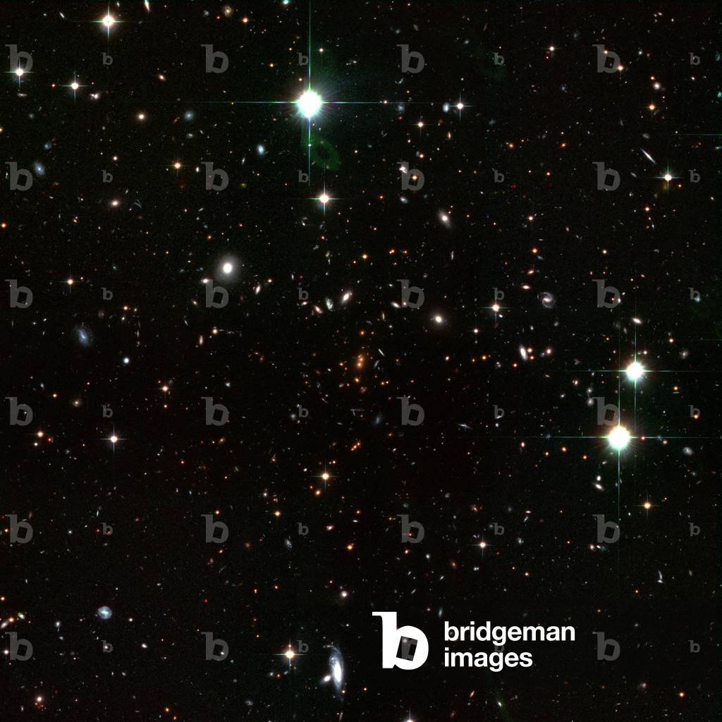 Clusters of distant galaxies RDCS1252.9 - 2927 - Distant galaxy cluster RDCS1252.9 - 2927 - This cluster of galaxies is 9 billion years old - light in the constellation Hydra, and is the most massive known to date. It probably contains several thousand galaxies. Image obtained by the Hubble Space Telescope and the VLT. The image shows the entire galaxy cluster (1/15 of a degree, corresponding to about 7 million light - years, across). The cluster probably contains many thousands of galaxies. Most of the other galaxies in the image, including most of the blue galaxies, are foreground or background galaxies. The image, which is made with an additional infrared exposure taken with the European Southern Observatory's Very Large Telescope, shows mature galaxies in a massive cluster that existed when the cosmos was 5000 million years old. The cluster, called RDCS1252.9 - 2927, is as massive as '300 trillion' suns and is the most massive known cluster for its epoch. Dominating the core are a pair of large, reddish elliptical galaxies [near centre of image]. Their red colour indicates an older population of stars. Most of the stars are at least 1000 million years old. The two galaxies appear to be interacting and may eventually merge to form a larger galaxy that is comparable to the brightest galaxies seen in present - day clusters. The red galaxies surrounding the central pair are also cluster members. The colour - composite image was assembled from two observations taken between May and June 2002 by the ACS Wide Field Camera, and one image with the ISAAC instrument on the VLT taken in 2002