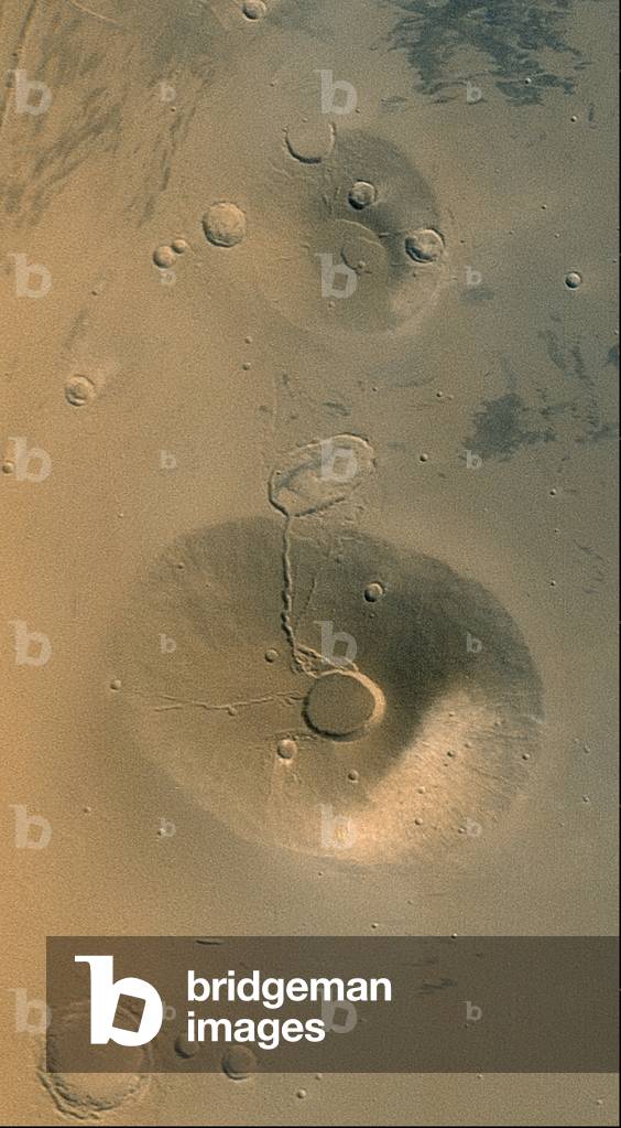 March - Volcanos Ceraunius Tholus and Uranius Tholus - Mars - Volcanos Ceraunius Tholus and Uranius Tholus - Image obtained by the Mars Global Surveyor probe in March 2002. This image shows the volcanoes Ceraunius Tholus (bottom) and Uranius Tholus (top). The presence of impact crateres on these volcanoes indicates that these volcanoes are old. The crater at the top of Ceraunius Tholus is about 25 km in diameter. Acquired in March 2002, this Mars Global Surveyor (MGS) Mars Orbiter Camera wide angle view shows the martian volcanoes, Ceraunius Tholus (lower) and Uranius Tholus (upper). The presence of impact craters on these volcanoes, particularly on Uranius Tholus; indicates that they are quite ancient and are not active today. The light - toned area on the southeastern face (towards lower right) of Ceraunius Tholus is a remnant of a once more extensive deposit of dust from the global dust storm events that occurred in 2001. The crater at the summit of Ceraunius Tholus is about 25 km (15.5 mi) across. Sunlight illuminates the scene from the lower left