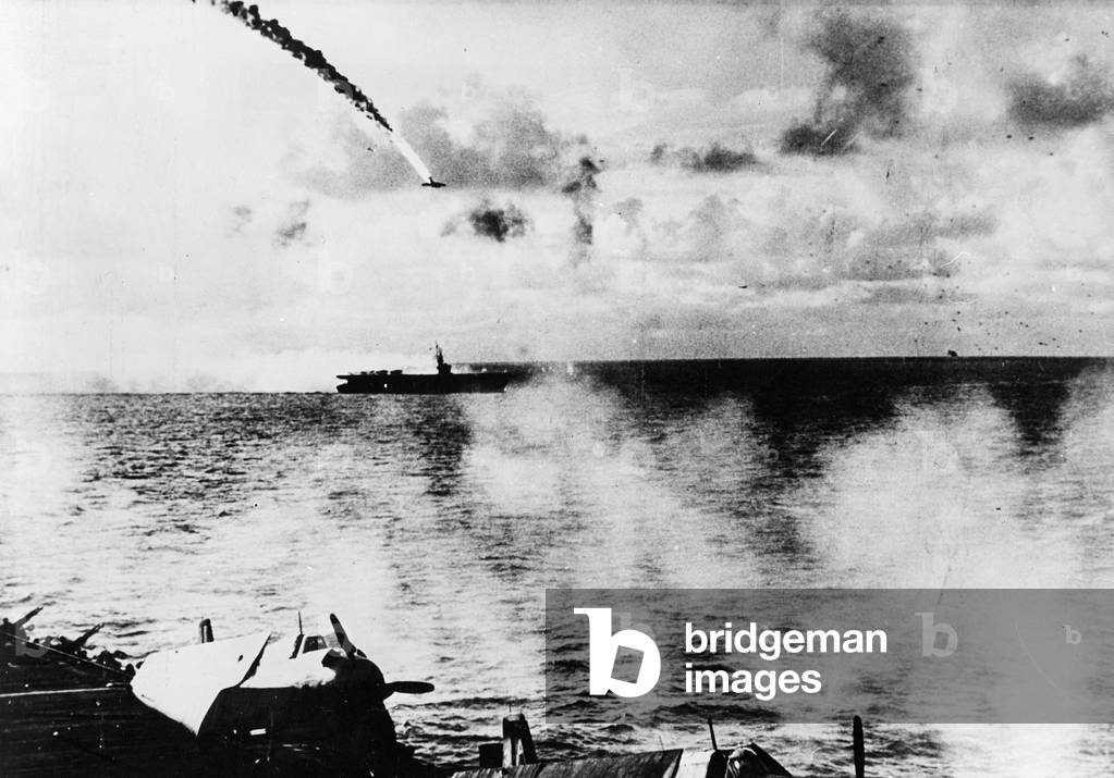 Japanese Kamikaze plane, on fire, dives towards a US aircraft carrier, 1940s (b/w photo)