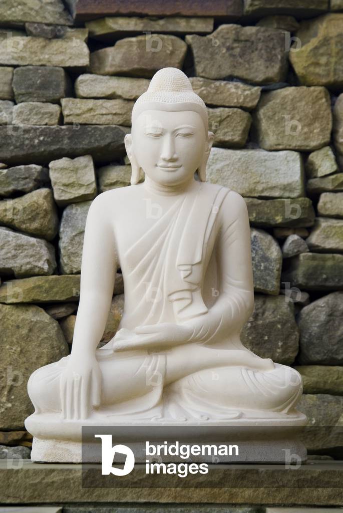 Buddha statue in full lotus position in front of dry-stone wall, Harnham Buddhist Monastery, Northumberland, UK (photo)