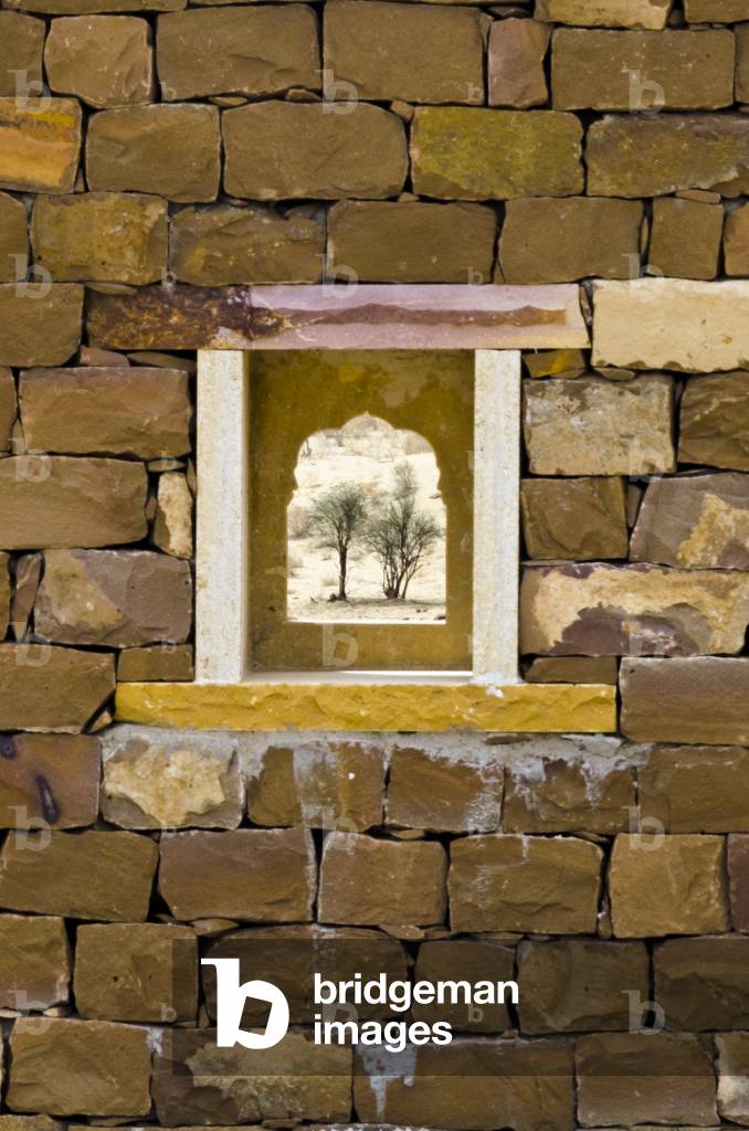 A small desert view through an arched window in a sandstone block wall at Khabha Fort, Thar Desert, Rajasthan, India (photo)