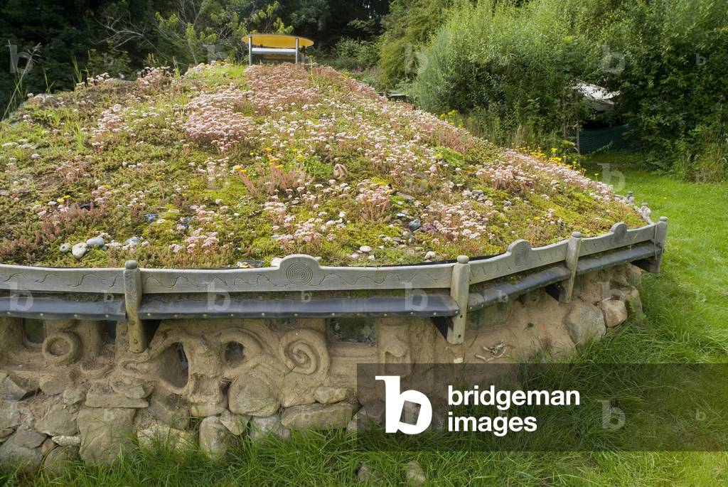Sustainable building: Low-impact roundhouse with ornate cob walls and flowering green roof in welsh woodland clearing 
South Wales, UK (photo)