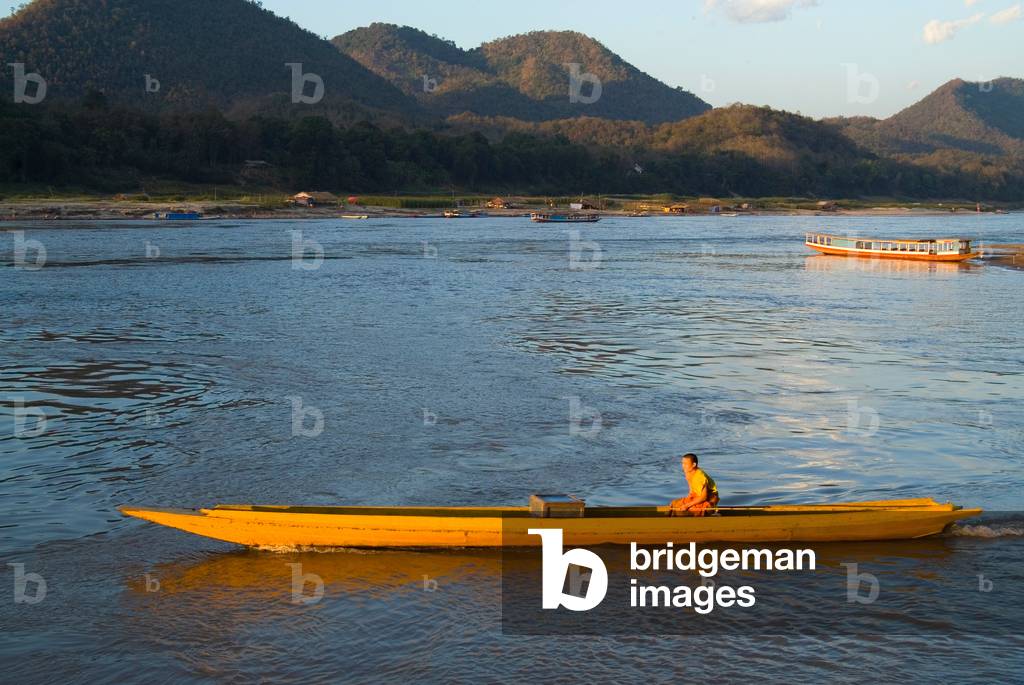 Buddhist monk steering longboat along the Mekong River (photo)