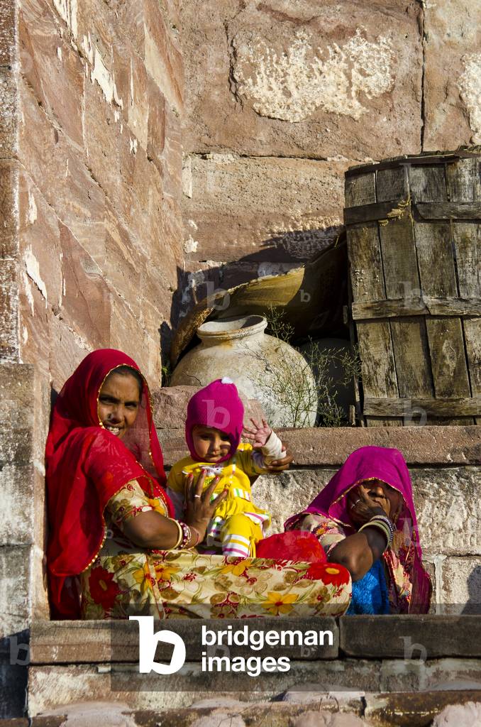 Two Indian women in colourful dresses and infant sitting on stone wall,
Mehrangarh Fort, Jodhpur, Rajasthan, India (photo)