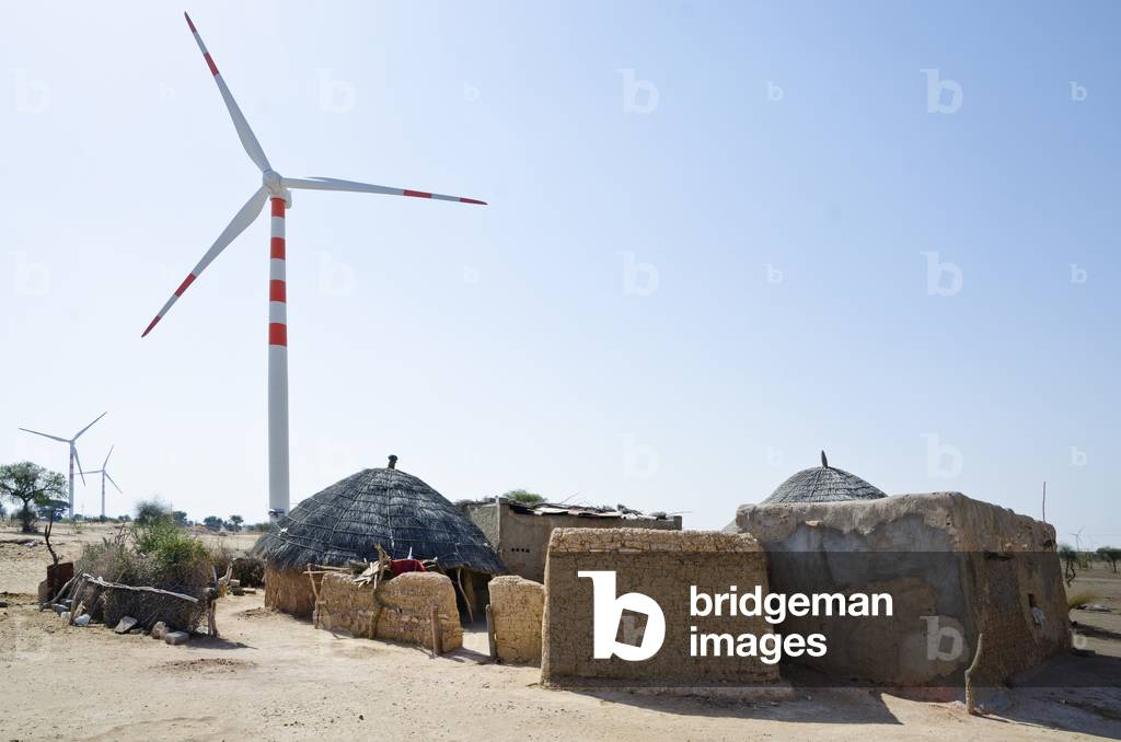 Wind turbines behind traditional huts in a Thar Desert village, Lakhmana, Rajasthan, India (photo)