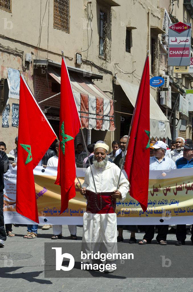 International Workers' Day: Elder leading parade carrying 3 Moroccan flags through medina of old Berber town, Taroudant, Souss-Massa-Draa Region, Morocco (photo)