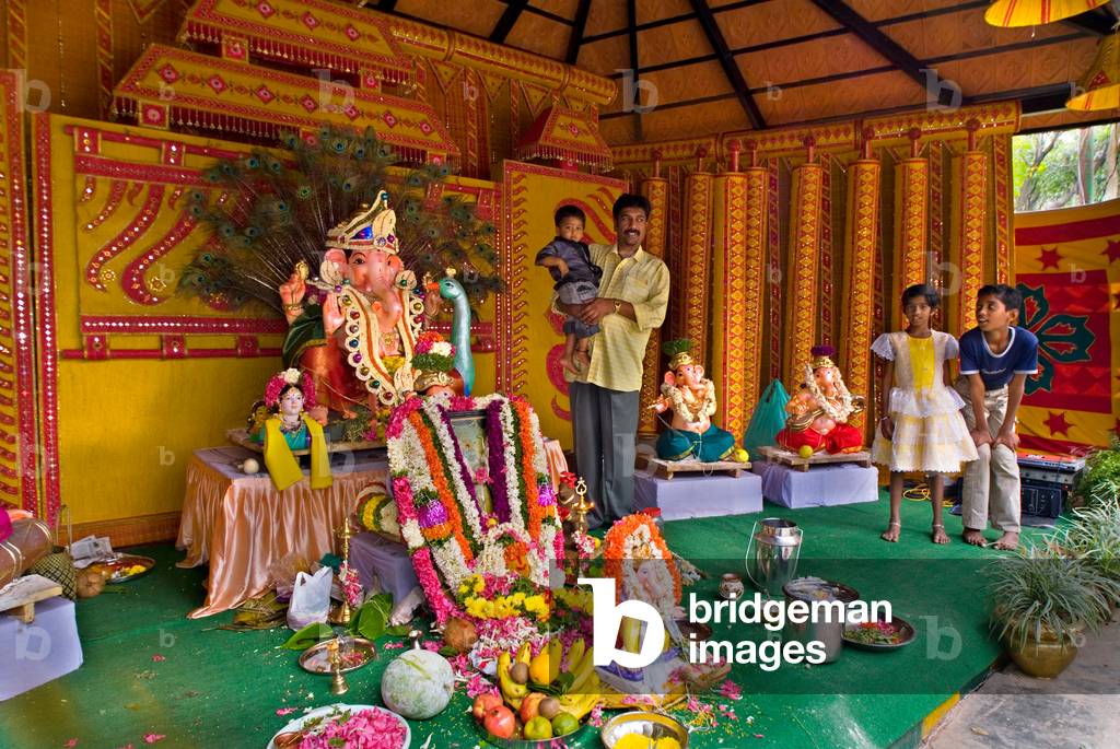 Father and children posing with Ganesh statue in shrine on the last day of the Ganesh Festival. 