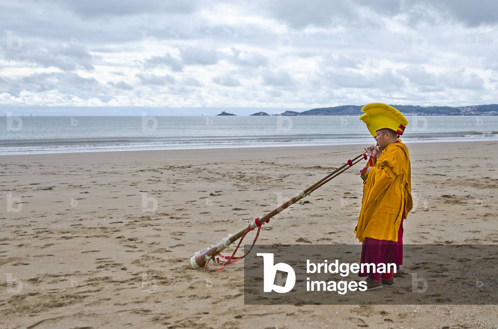 Tibetan Buddhist monks in ceremonial dress blowing Tibetan horns on Swansea beach during a fundrasing visit to the UK, Swansea, South Wales (photo)