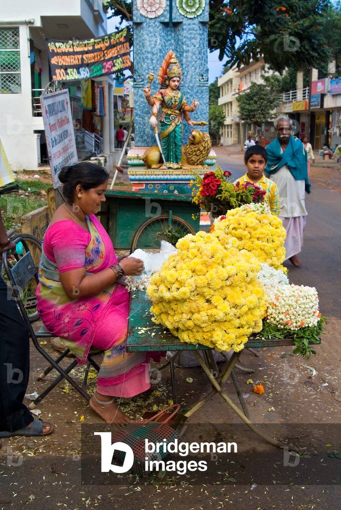 Flower garland maker and seller sitting under Durga Devi temple arch in Vidyaranyapura, Bangalore, Karnataka, India
