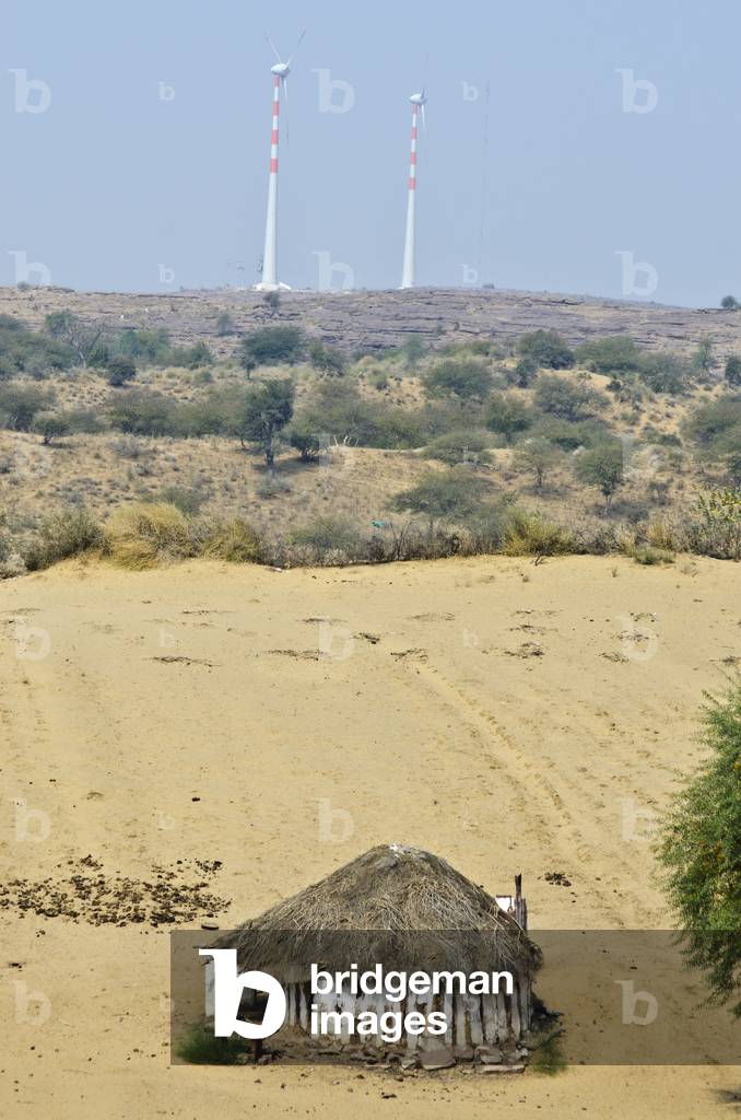 Thatched round hut in desert sanddunes in front of large wind tubines on hill,
Keralha Bakhar, Rajasthan, India (photo)